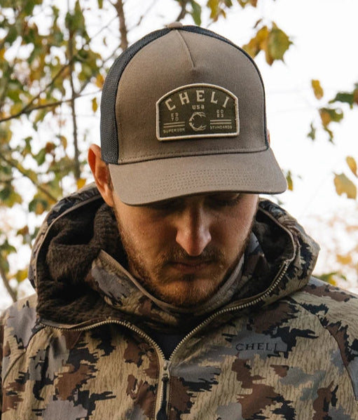 Person in outdoor clothing crouching in a wooded area.