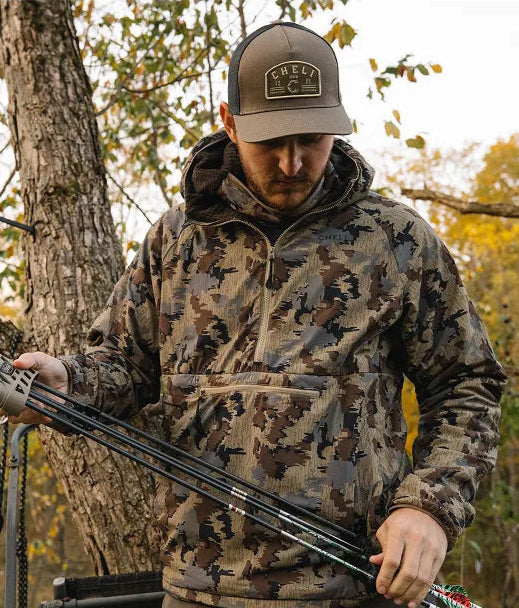 Person in outdoor clothing crouching in a wooded area.