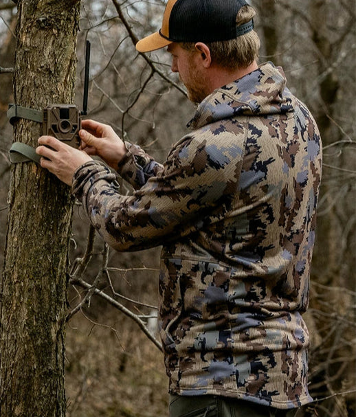 Man in camouflage setting up a trail camera on a tree.